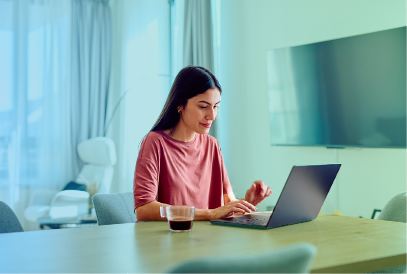 An employee is sitting at their desk at home, taking an engagement survey and smiling at the laptop on their desk.