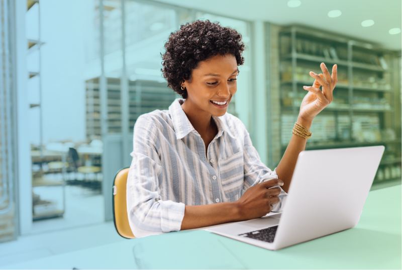 An employee is sitting at their desk, looking at their laptop and smiling.
